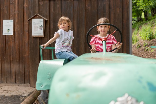 Zwei Mädchen auf dem Traktor vor Scheune